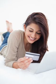 A close up shot of a woman reading her credit card while in front of her tablet.