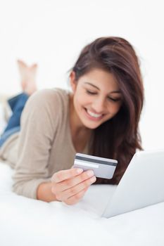 A close up focus shot on the credit card that the smiling woman is holding as she uses her tablet.