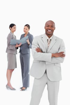 Smiling salesman with arms crossed and co-workers behind him against a white background