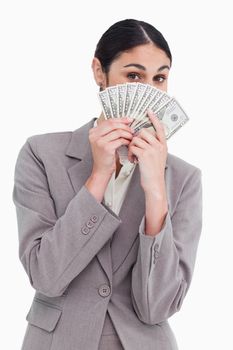 Young saleswoman hiding her face behind bank notes against a white background