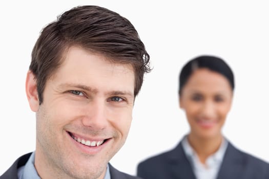 Close up of smiling salesman with colleague behind him against a white background
