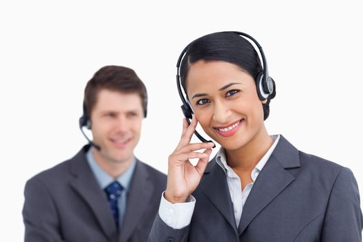 Close up of smiling call center agent with colleague behind her against a white background
