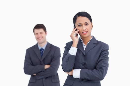 Close up of serious saleswoman on the phone with co-worker behind her against a white background