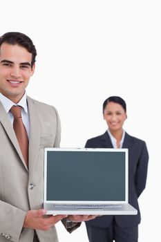 Laptop being presented by smiling salesman with colleague behind him against a white background