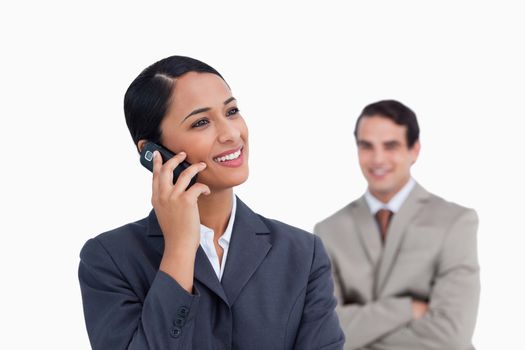 Smiling saleswoman on her mobile phone and co-worker behind her against a white background