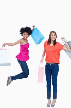 A teenage girl leaping while holding her shopping bags while her friend is smiling