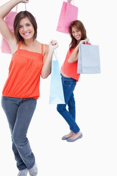 Teenager followed by a friend and both are holding shopping bags while smiling