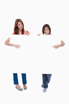 Smiling teenagers showing the blank poster while pointing their fingers on it