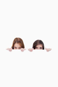 Two friends secretly hiding behind a blank poster against a white background