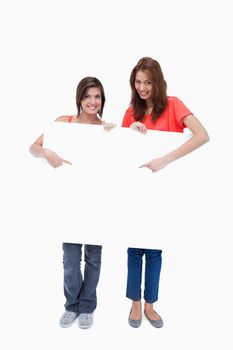 Teenagers smiling and standing behind a blank poster while pointing it