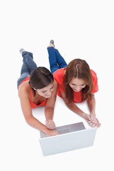 Smiling teenagers lying down while attentively looking at a computer