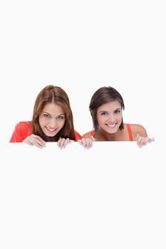 Smiling teenagers holding a blank poster while hiding behind it