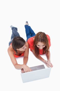 Smiling teenage looking at her friend and lying down while using a laptop