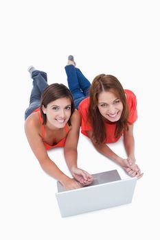 Beautiful teenagers lying down with a laptop while looking at the camera