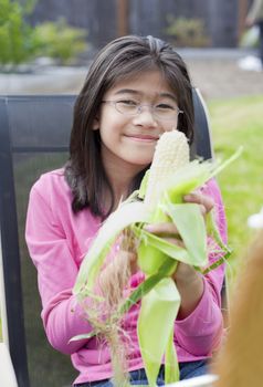 Girl peeling husk off corn cob outdoors