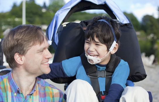 Father and disabled five year old son laughing together on beach