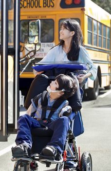 Ten year old girl  pushing disabled little boy wearing protective gear  in wheelchair  next to school bus. Child has cerebral palsy.