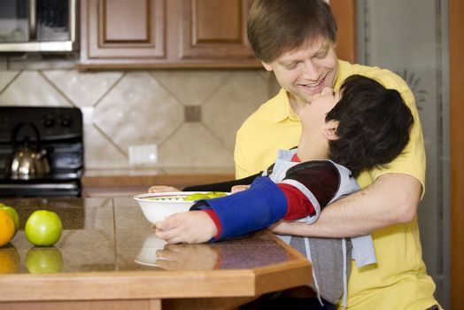 Father helping disabled son putting fruit into bowl in the kitchen. Son has cerebral palsy.