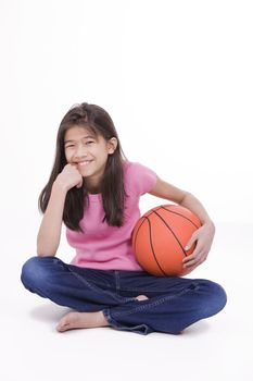 Ten year old Asian girl sitting on floor holding basketball, isolated on white