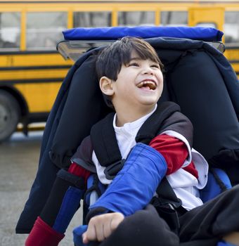 Disabled five year old boy in wheelchair, by schoolbus
