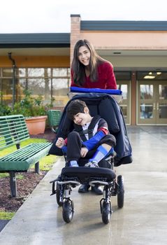 Teenage girl pushing her  little disabled brother in wheelchair leaving school