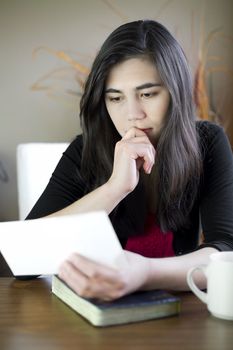 Biracial teenage girl or young woman reading  note in hand with worried or sad expression