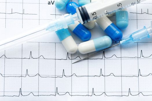 Syringe and tablets on the paper with graph of heart rhythm