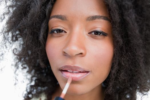 Young woman using a lip gloss applicator to make-up against a white background
