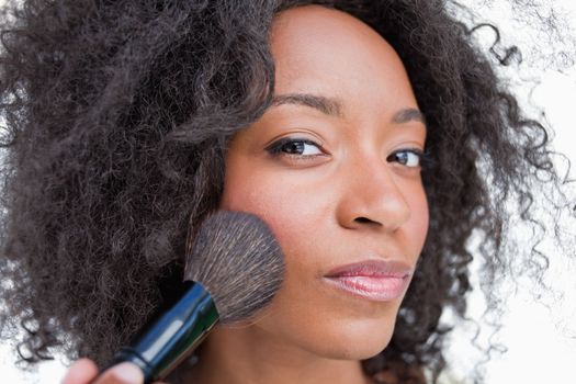 Young serious woman applying blush with powder brush against a white background