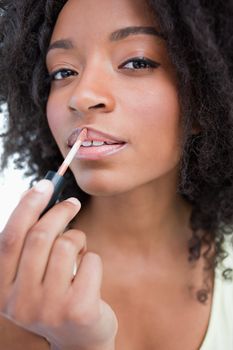 Young woman applying gloss in a concentrated way against a white background