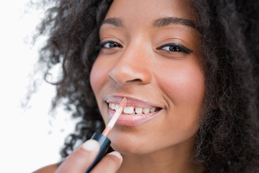 Woman making-up while using a lip gloss applicator against a white background