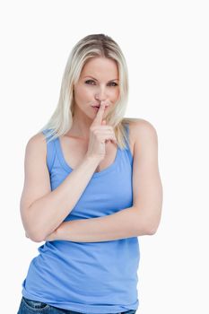 Blonde woman telling to be quiet with her arms crossed against a white background