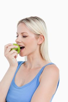 Beautiful blonde woman eating a green apple against a white background