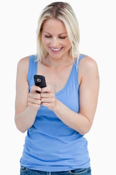 Smiling blonde woman sending a text with her cellphone against a white background