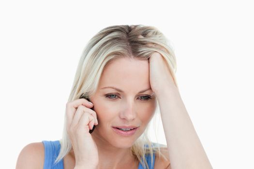 Serious blonde woman talking on cellphone with her hand on her forehead