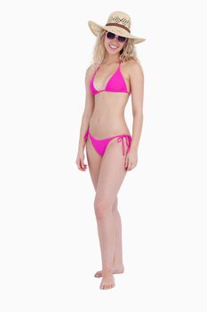 Woman wearing pink swimsuit with a hat and sunglasses while standing upright