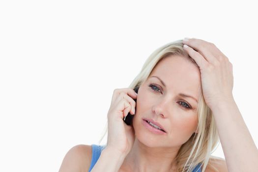 Serious blonde woman talking on the phone while placing her hand on her head