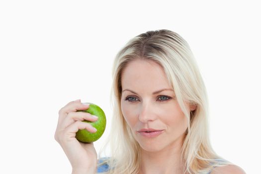 Thoughtful blonde woman holding a green apple against a white background