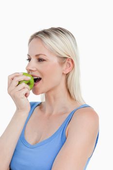 Blonde looking to the side while eating a green apple against a white background