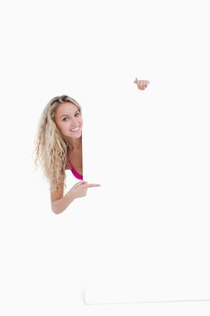 Beautiful teenage showing a great smile while pointing her finger at a blank poster