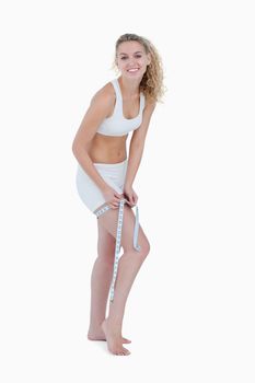 Smiling young blonde woman measuring her thigh against a white background