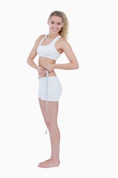 Smiling teenager standing up while measuring her waist against a white background