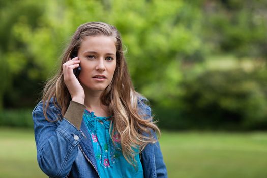 Young serious woman talking on the phone while standing in the countryside
