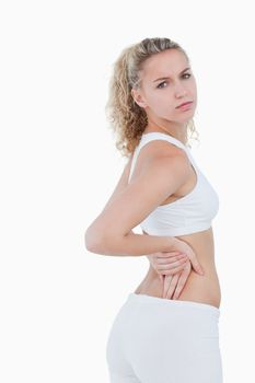 Young serious woman showing a pain in the back against a white background