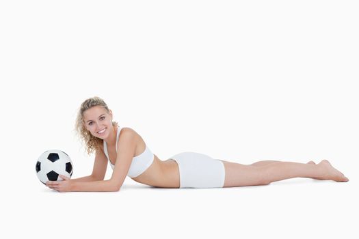 Smiling woman lying down while holding a football against a white background