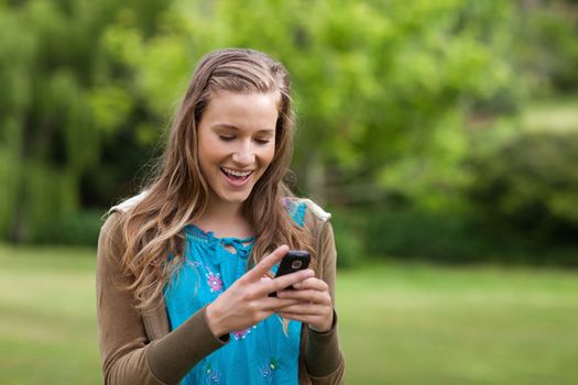 Happy teenage girl receiving a text on her mobile phone while standing in a park