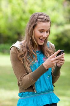 Teenager receiving a surprising text on her mobile phone while standing in a park