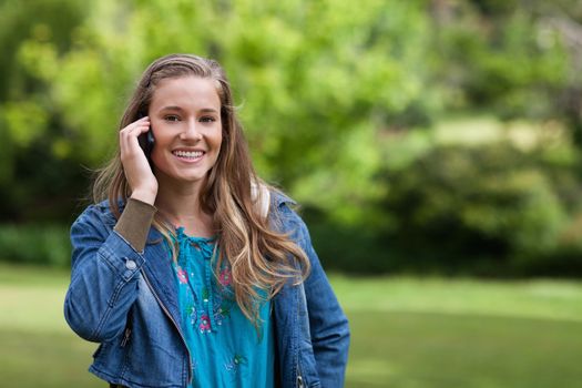 Smiling teenager using her mobile phone while standing in a park