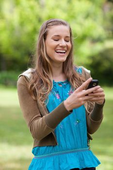 Laughing teenager standing in a park while receiving a text on her mobile phone 