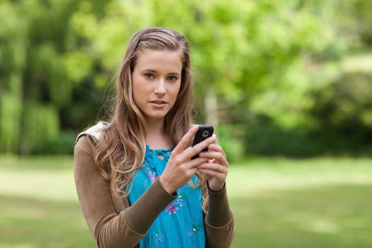 Teenager sending a text while standing in a park and looking at the camera